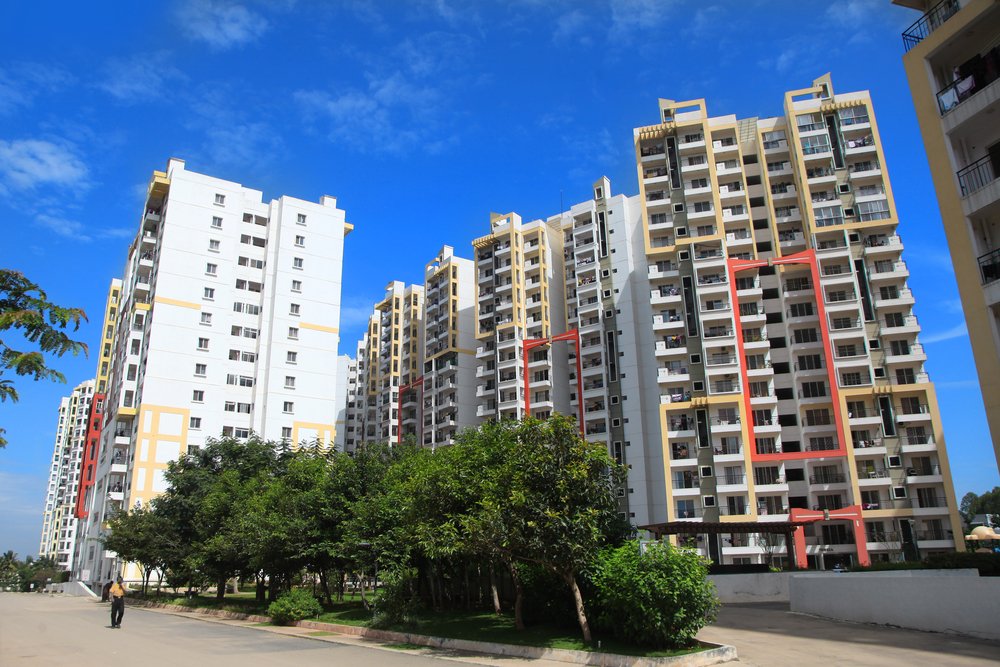 A man walking on a sidewalk past a row of apartment buildings with trees in front of them.